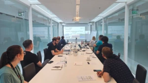 A group of people sitting around a long white table in a glass-walled conference room. A presentation about "PoliTO - Politecnico di Torino" is projected onto the front screen.
